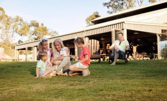 a family of five , including a mother , father , and two children , is sitting on the grass in a park , enjoying each other 's at Paradise Country Farmstay