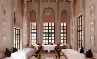 A restaurant with white tables and chairs is located in front, while large windows are situated on the far side at Amanbagh