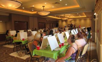 a group of people are sitting at tables , painting while using their computers in an art class at The Inn at Charles Town / Hollywood Casino