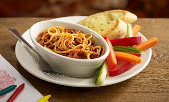 a white bowl filled with spaghetti , accompanied by a variety of vegetables and bread on a dining table at Premier Inn Bangor (Gwynedd, North Wales)