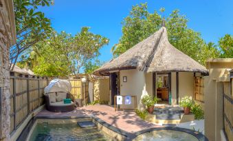 a small house with a thatched roof is surrounded by a wooden fence and has a hot tub in the backyard at Banyan Tree Vabbinfaru