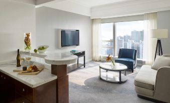 The living room features large windows and is furnished with a couch and chair, both facing the television at Cordis, Hong Kong