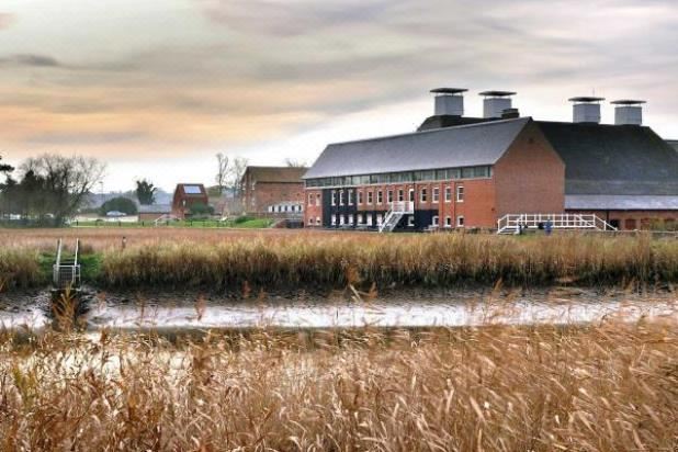 a large brick building with a brown roof and two tall , white towers is surrounded by tall grasses at YHA Blaxhall - Hostel