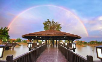 a wooden bridge with a thatched roof , surrounded by trees and a rainbow in the background at Mane Hariharalaya