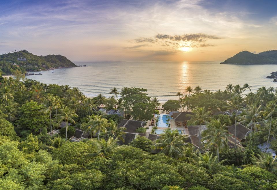 a tropical resort with a pool surrounded by lush greenery and palm trees , overlooking the ocean at sunset at Anantara Rasananda Koh Phangan Villas