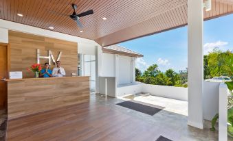 a reception area with a wooden counter , two people behind it , and an open doorway leading to a balcony with trees in the background at Anantara Rasananda Koh Phangan Villas