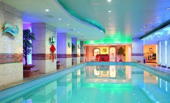 a large indoor swimming pool with blue lights and a white tiled floor , surrounded by buildings and greenery at Phoenix Hotel