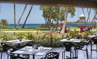 an outdoor dining area overlooking the ocean , with several tables and chairs arranged for guests to enjoy a meal at Chateau Royal Beach Resort & Spa, Noumea