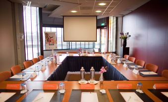 a conference room set up for a meeting , with multiple tables and chairs arranged in a semicircle at Leonardo Hotel Lelystad City Center