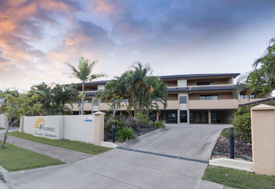 a modern apartment building surrounded by palm trees and a driveway leading up to it at Windmill Motel and Events Centre