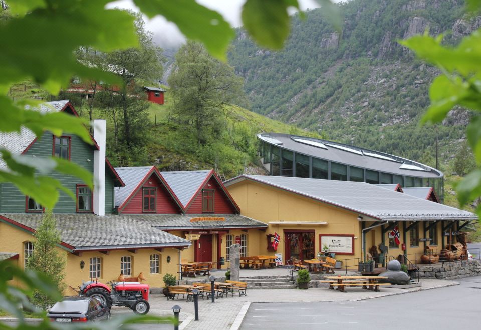 a small village with a yellow building and a red barn , surrounded by mountains and greenery at Byrkjedalstunet Hotell