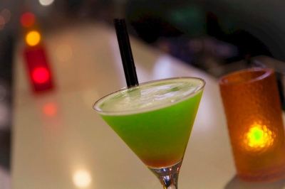 a cocktail with a green and yellow color is being stirred with a black straw at Ibis Melbourne Hotel and Apartments