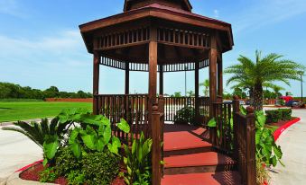 a wooden gazebo surrounded by greenery , with a red carpet leading up to it at La Quinta Inn & Suites by Wyndham Houston Channelview