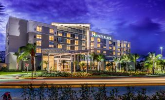 a large hotel building surrounded by palm trees , with the hotel 's name displayed on the building at Hyatt Place Manati