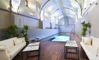 a modern , open - air indoor space with a swimming pool and wooden flooring , featuring white sofas and tables arranged around the space at Parador Monasterio de Corias