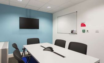 a conference room with a white table , black chairs , and a television mounted on the wall at Super 8 by Wyndham Chester East