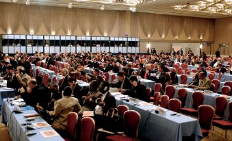 a large group of people are seated in rows of tables at a conference , with the floor set up for a discussion at Kobe Portopia Hotel