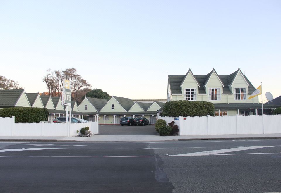 a row of green and white buildings with a street in front of them , under a clear blue sky at Asure Green Gables Motel