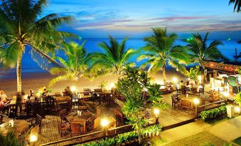 a tropical resort with palm trees , lit up by lights , and a wooden deck extending from the ocean at Chaolao Cabana Resort