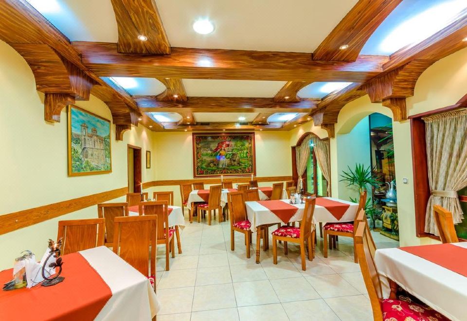 a restaurant with wooden tables and chairs , red tablecloths , and paintings on the walls , under a high ceiling at Hotel Cosmos