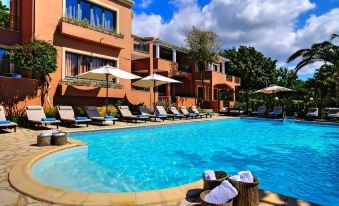 a beautiful swimming pool area with umbrellas , sun loungers , and trees in front of a red - brick building under a blue sky at Lena Mare Boutique Hotel