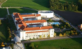 an aerial view of a large white building surrounded by green fields and a body of water at The Monarch Hotel