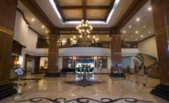 a grand hotel lobby with a grand piano in the center , surrounded by chairs and tables at The Sunan Hotel Solo