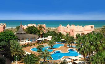 a resort with a large pool surrounded by palm trees , and a view of the ocean in the background at Oliva Nova Beach & Golf Hotel