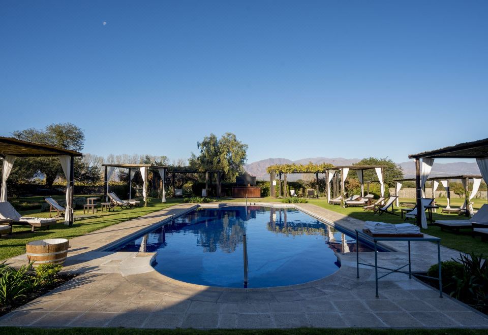 a large , circular swimming pool is surrounded by lounge chairs and a pergola in a sunny outdoor setting at Patios de Cafayate