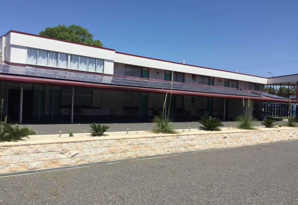 a modern building with a red roof and large windows is surrounded by gravel and plants at Ambassador Motel