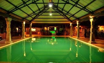 a large indoor swimming pool surrounded by green grass , with people enjoying their time in the water at Aalankrita Resort and Convention