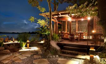 a wooden deck with tables and chairs , surrounded by rocks and trees , illuminated by outdoor lights at night at Jicaro Island Lodge Member of the Cayuga Collection