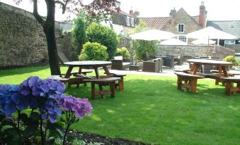 a well - maintained garden with green grass , wooden benches , and umbrellas , as well as a house in the background at The George at Nunney