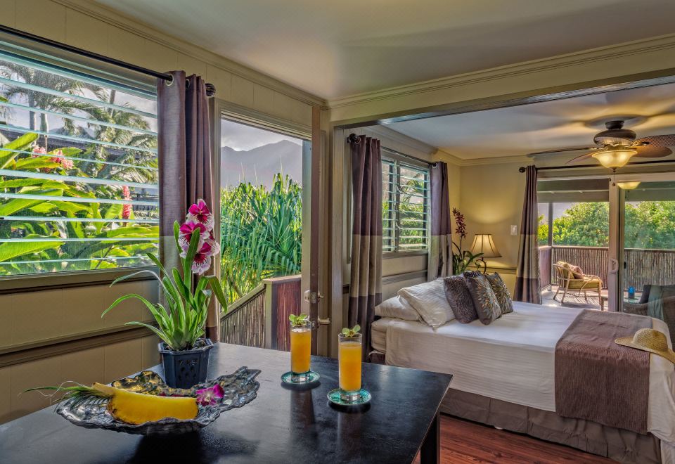 a bedroom with a bed , table , and plants is shown with large windows overlooking a garden at Paradise Bay Resort