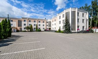 a large , modern building with a white facade and red arches , situated in an open area with parking spaces at Hotel Boss