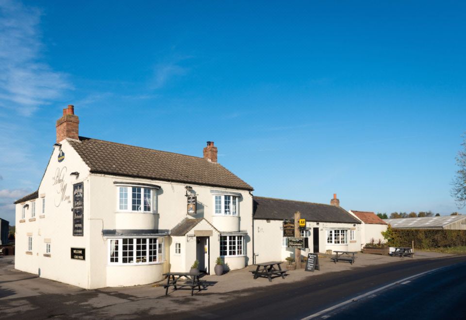 a white building with a thatched roof and black trim is situated on a street corner at The Blackamoor Inn