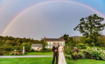 a newlywed couple stands in front of a house with a rainbow in the background at Blueberry Hill Inn