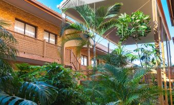 a tropical courtyard with tall plants and a covered walkway , surrounded by wooden buildings on both sides at Quality Hotel Robertson Gardens