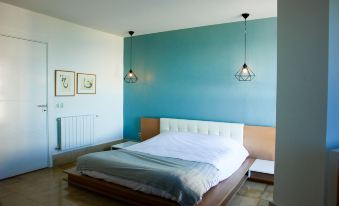 a modern bedroom with blue walls , white bedding , and two pendant lights hanging above the bed at The View Gammarth