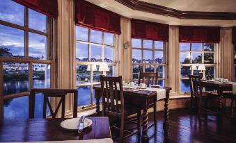 a dining room with a table set for two , surrounded by large windows overlooking a body of water at Small Luxury Hotels of the World - the Mitre Hampton Court
