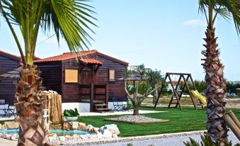 a wooden house with a red roof , surrounded by green grass and palm trees , under a clear blue sky at Hotel Neptuno