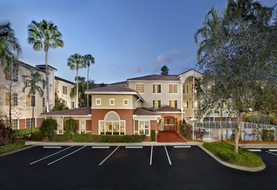 a large , modern apartment building with multiple balconies and parking spaces , surrounded by palm trees and clear skies at Residence Inn Fort Lauderdale Weston