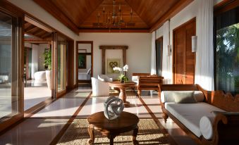 a spacious living room with wooden furniture , including a couch , chairs , and a dining table at Como Parrot Cay