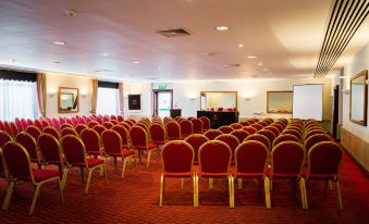 a conference room with rows of red chairs and a stage at the front , ready for a meeting or presentation at The Dragon Hotel