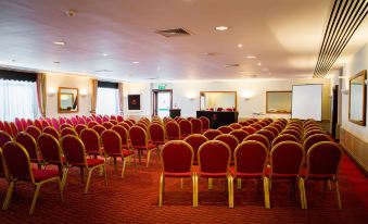 a large , empty conference room with rows of red chairs and a stage at the end at The Dragon Hotel