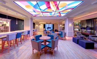 a modern lounge area with blue and yellow chairs , a large glass ceiling , and colorful geometric designs at El Fuerte Marbella