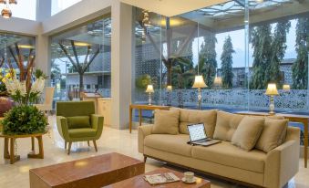 a modern living room with a couch , chairs , and a laptop on a table , surrounded by windows that offer a view of the outdoors at Hotel Horison Gkb Gresik