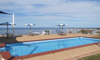 a large swimming pool with a view of the ocean and several lounge chairs and umbrellas at Stansbury Holiday Motel