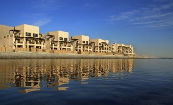 a row of modern apartment buildings on the shore of a body of water , with the reflection of the sky in the water at Atana Musandam Resort