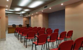 a conference room with rows of red chairs arranged in a semicircle , and a podium at the front of the room at Hotel Italia